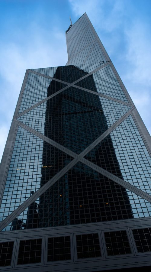 A low angle shot of a tall skyscraper in a glass facade with the reflection of another skyscraper in Hong Kong